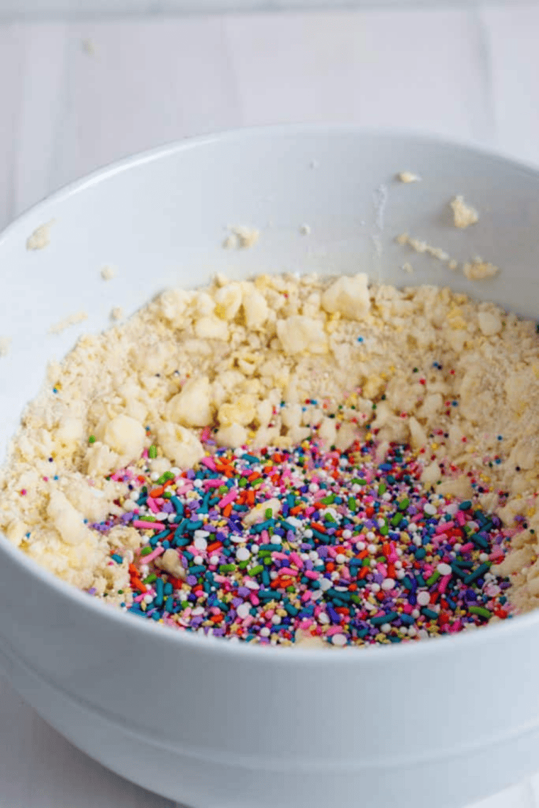 Hand-folding sprinkles into confetti cookie dough, with extra sprinkles in a small bowl.