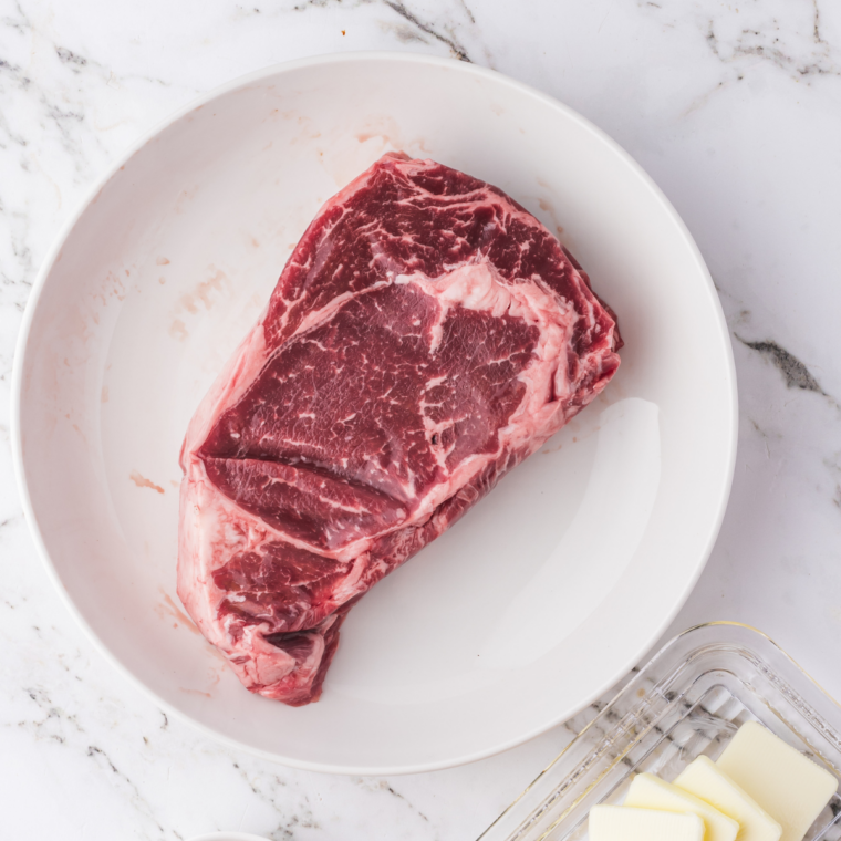 Raw ribeye salted on both sides resting uncovered on a wire rack for dry brining
