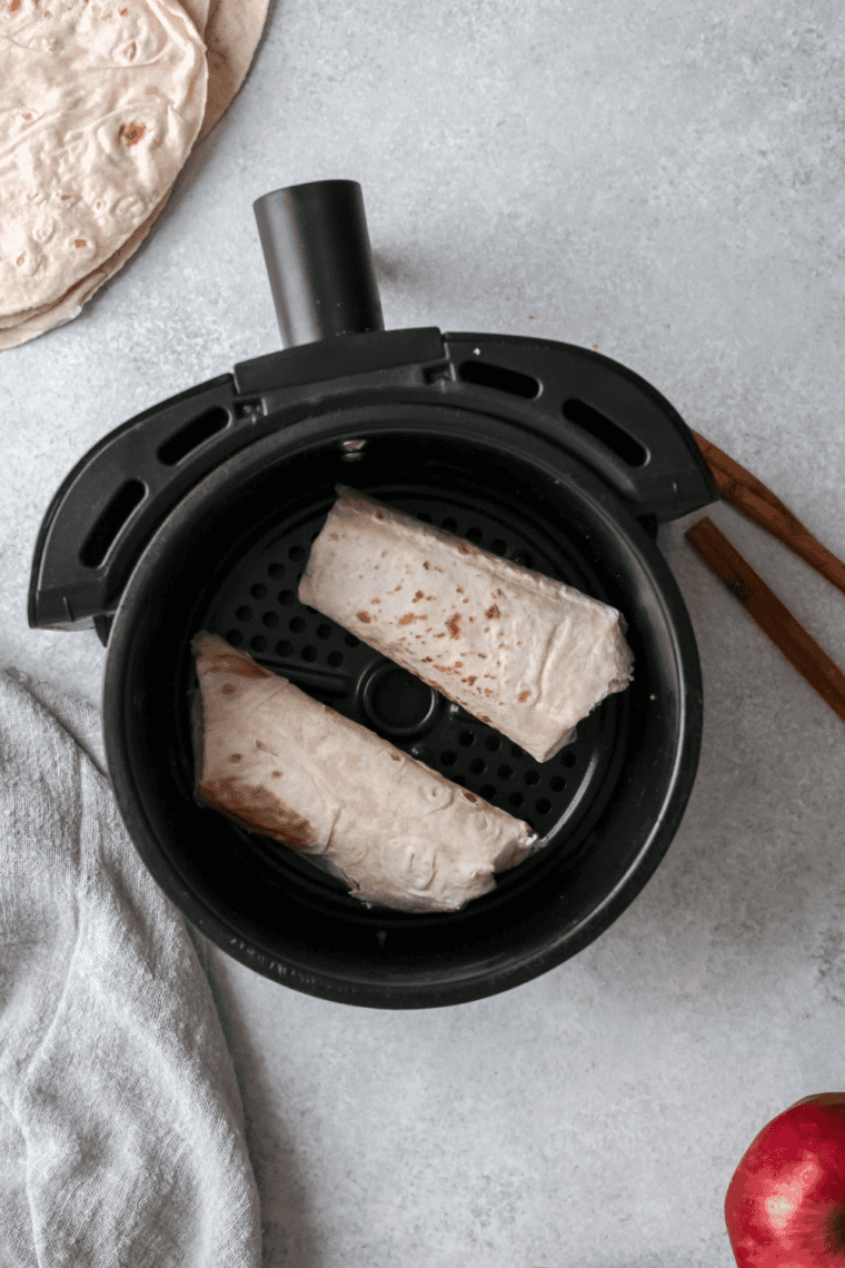 Crispy apple pie taquitos arranged in an air fryer basket after cooking