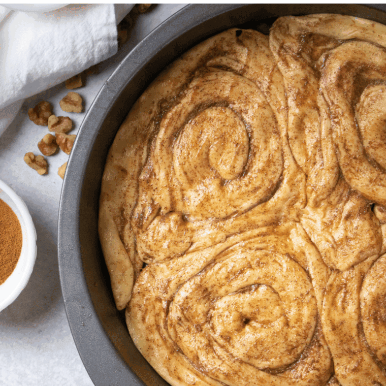 Sprinkling cinnamon sugar over apple pie filling layered on cinnamon roll crust in air fryer pan