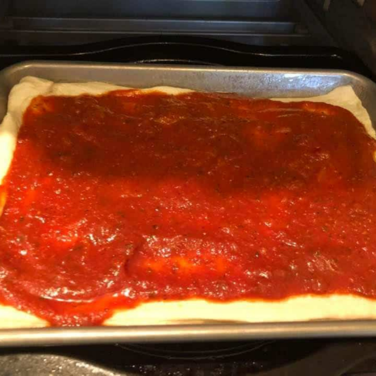 Sheet pan pizza dough docked with a fork and topped with a thin layer of red sauce