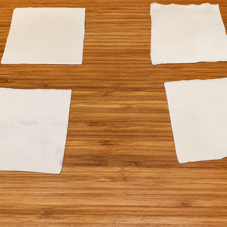 Square wonton wrappers laid out in rows on a wooden cutting board, ready to fill