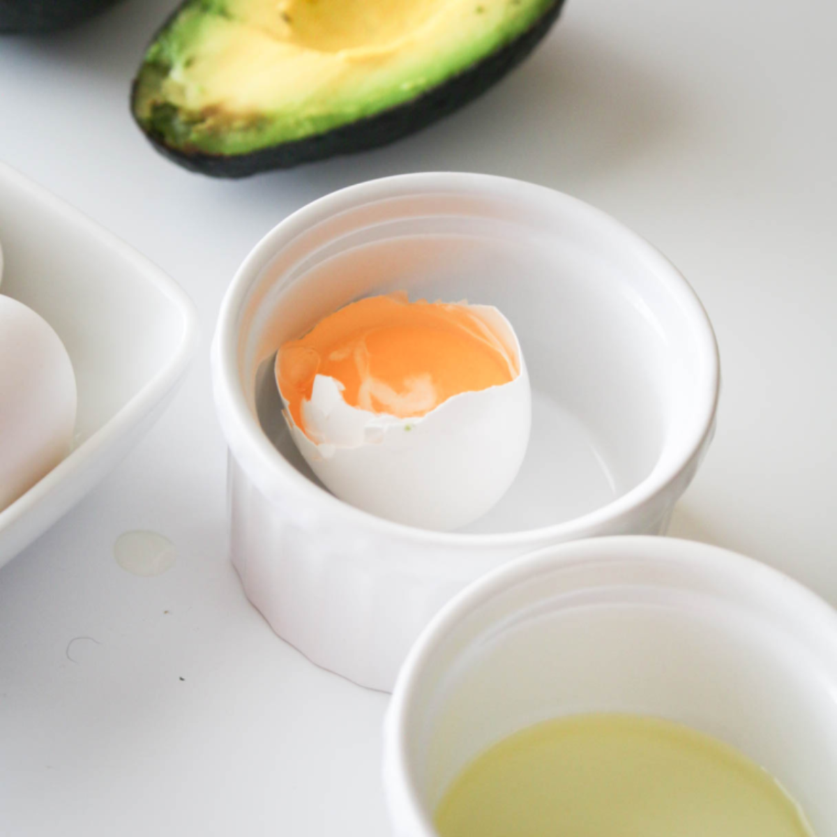 closeup: a cracked egg with a yolk in a white ramekin for air fryer avocado egg"