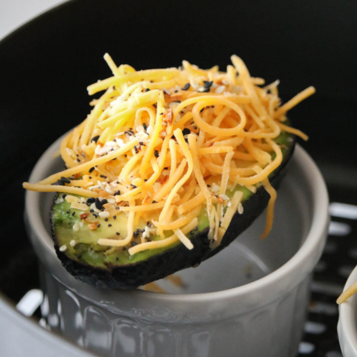 Air fryer avocado halves filled with cooked eggs, garnished with herbs, served on a plate.