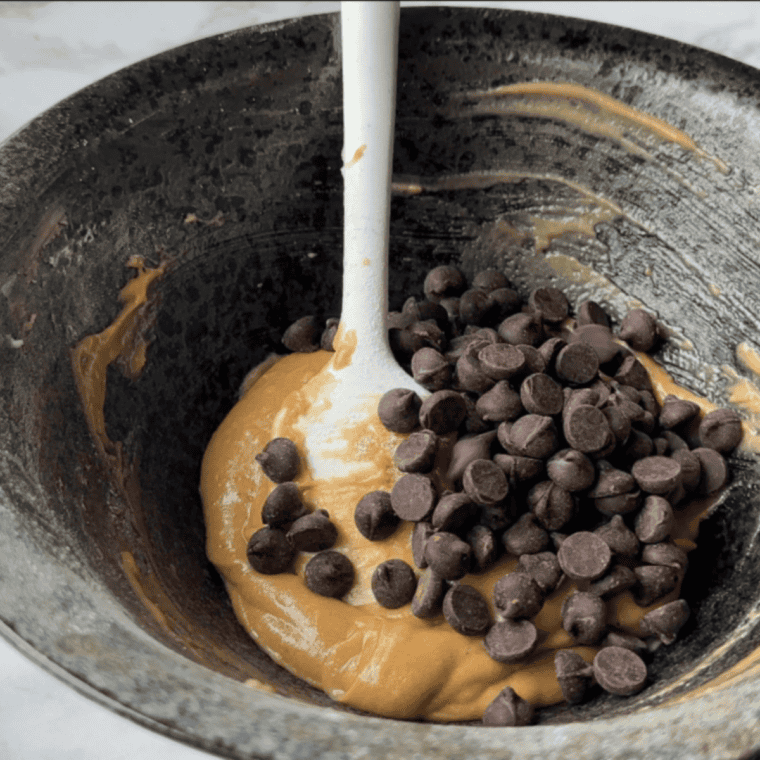 Mixing oatmeal chocolate chip cookie dough in a large bowl with flour, sugar, eggs, and chocolate chips.