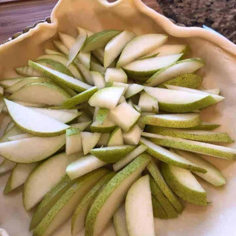 Thinly sliced pears piled in the center of pie dough with a bare border left around the edge for folding