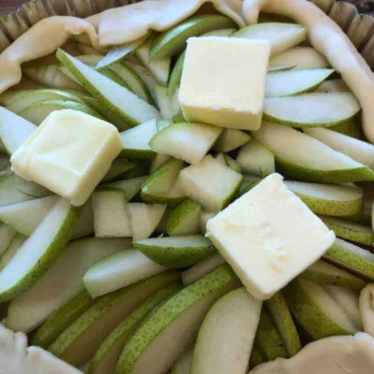 Pats of unsalted butter scattered over sliced pears inside pleated, folded galette crust