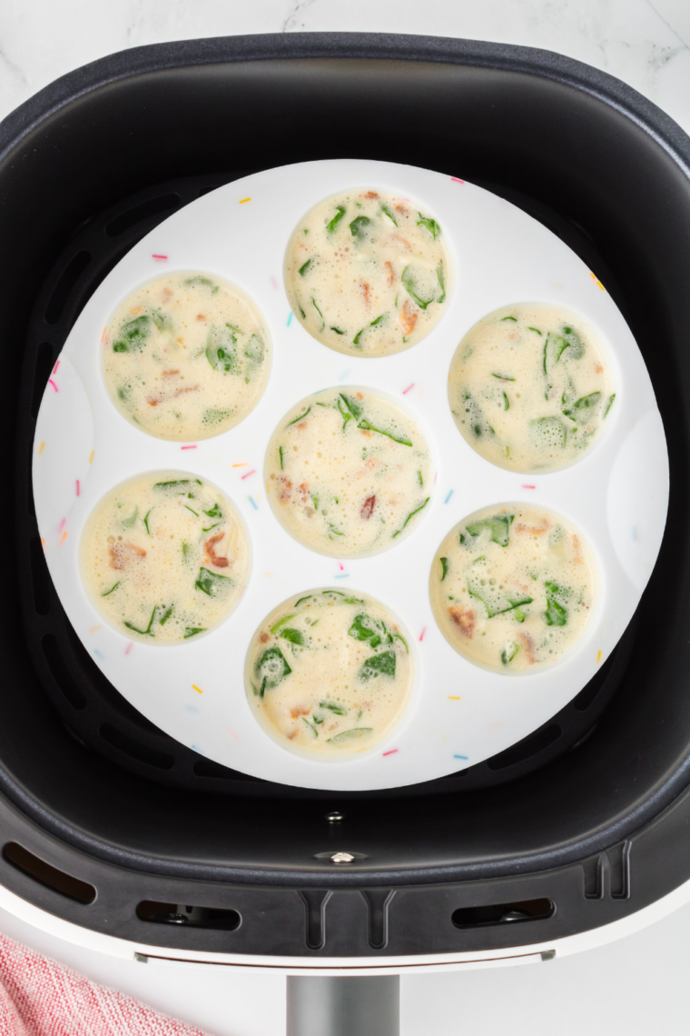 Air fryer basket with filled silicone molds cooking soft, fluffy egg bites.