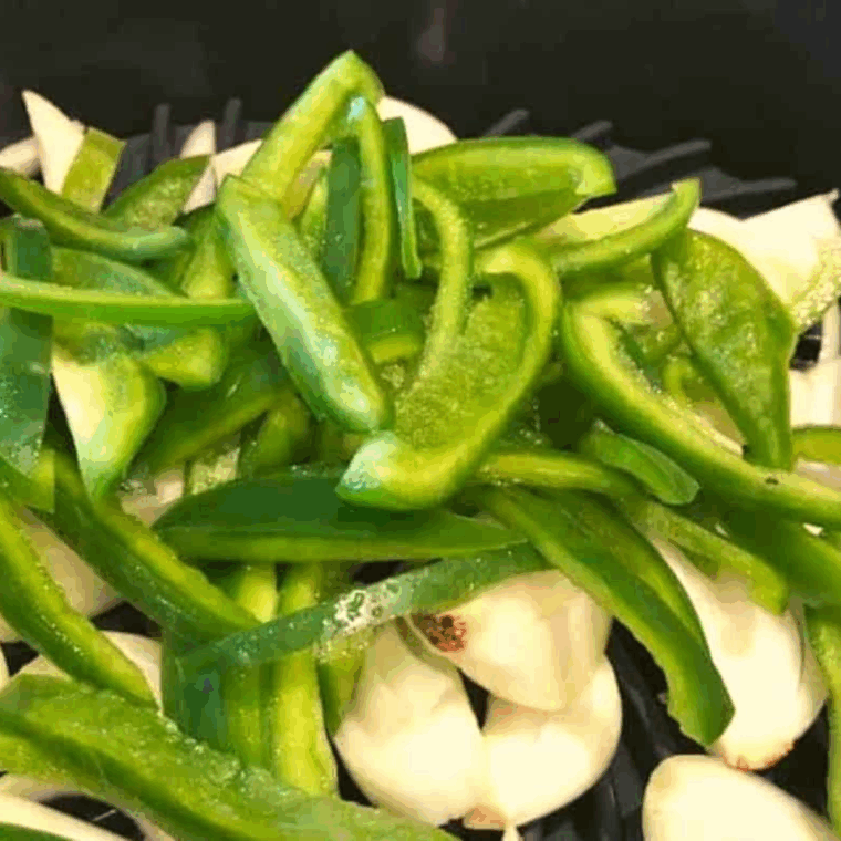 Sliced onions and bell peppers in a bowl coated with olive oil, ready for cooking.