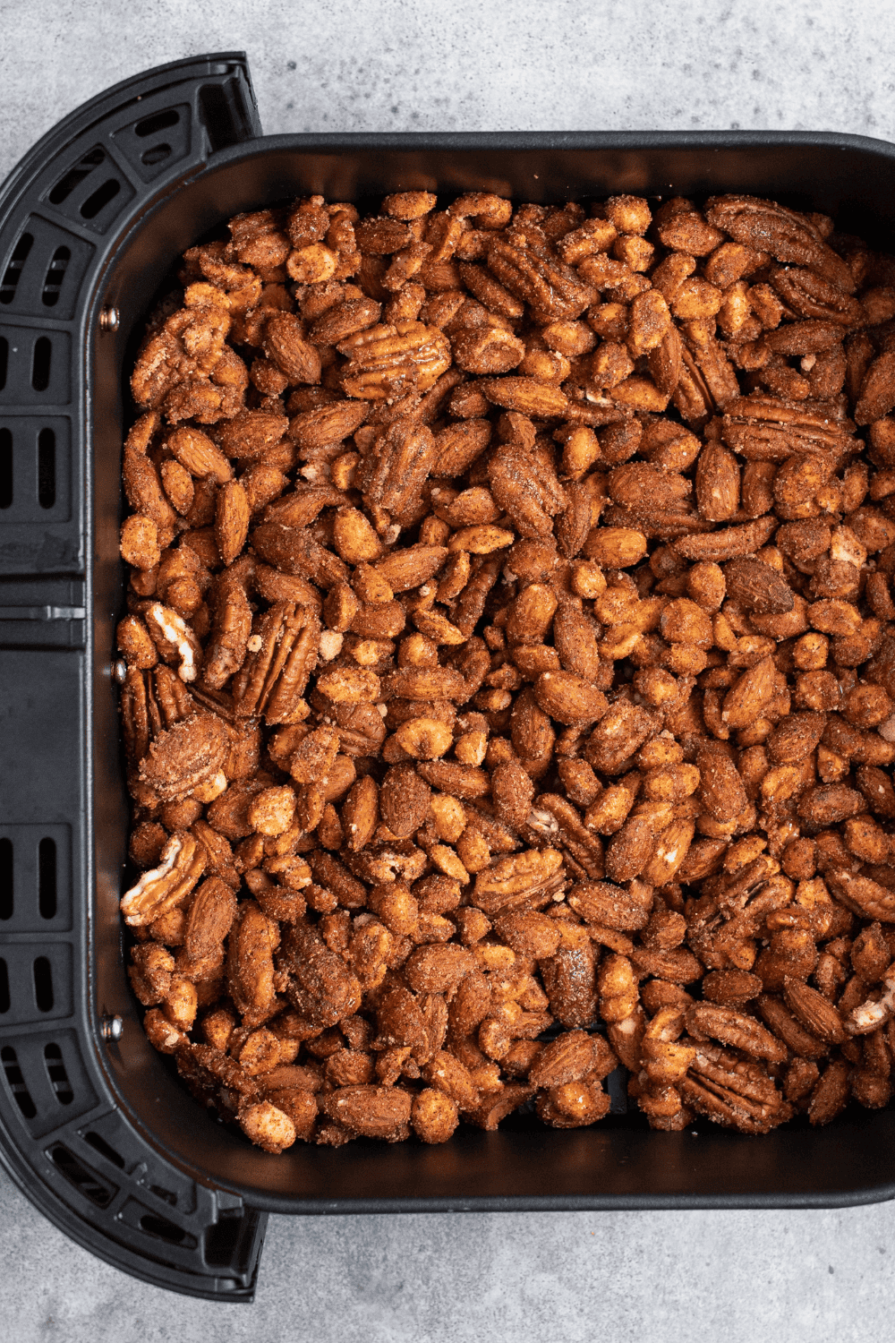 Seasoned mixed nuts spread in a single layer in an air fryer basket