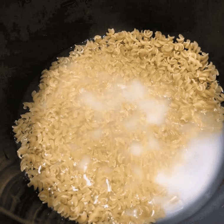 Dry macaroni noodles being poured into Instant Pot with water and milk.
