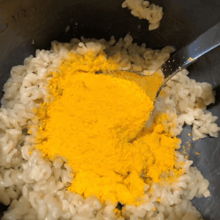 Butter, milk, and orange cheese powder being stirred into cooked macaroni.