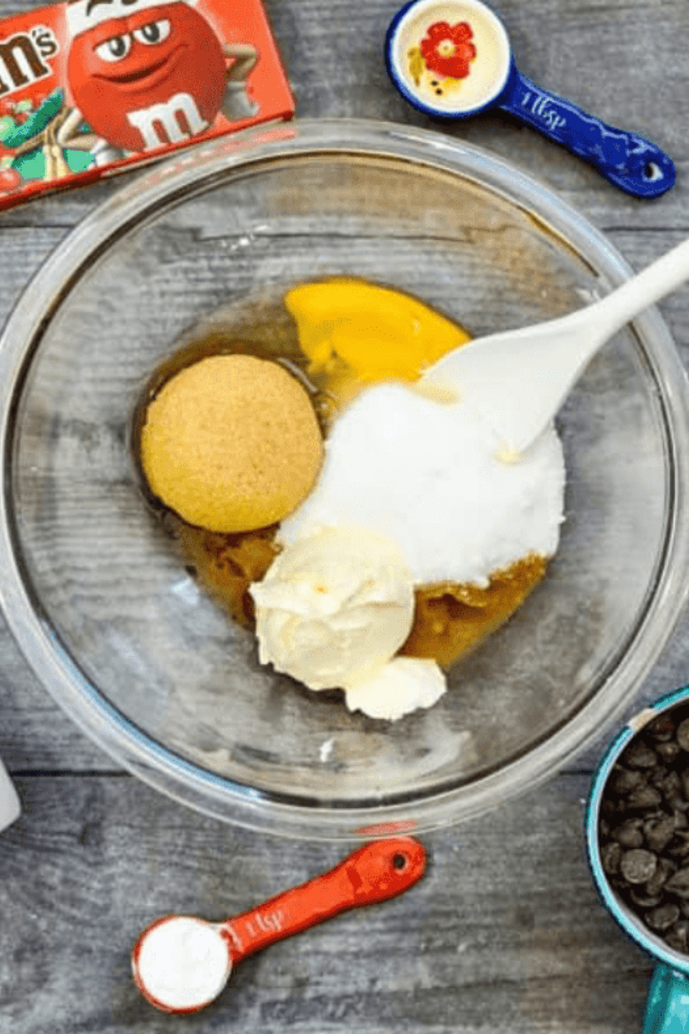 mixing cookie dough with butter, sugars, eggs, flour, chocolate chips, and M&M candies in a bowl