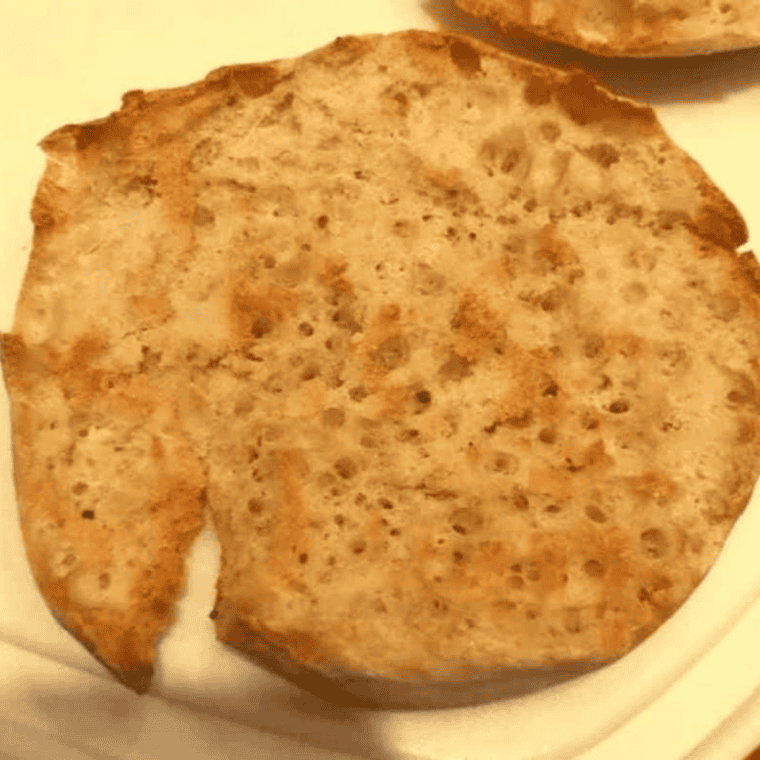 English muffin halves in an air fryer basket being toasted at 320&deg;F.