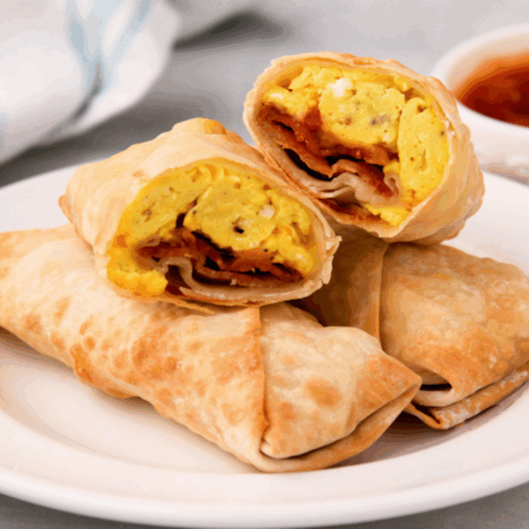 Crispy golden Air Fryer Breakfast Egg Rolls cut in half, showing the filling of scrambled eggs, sausage, and cheese, served with a side of salsa.