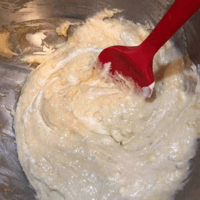Mixing donut batter thoroughly, scraping the sides of the bowl for even consistency.