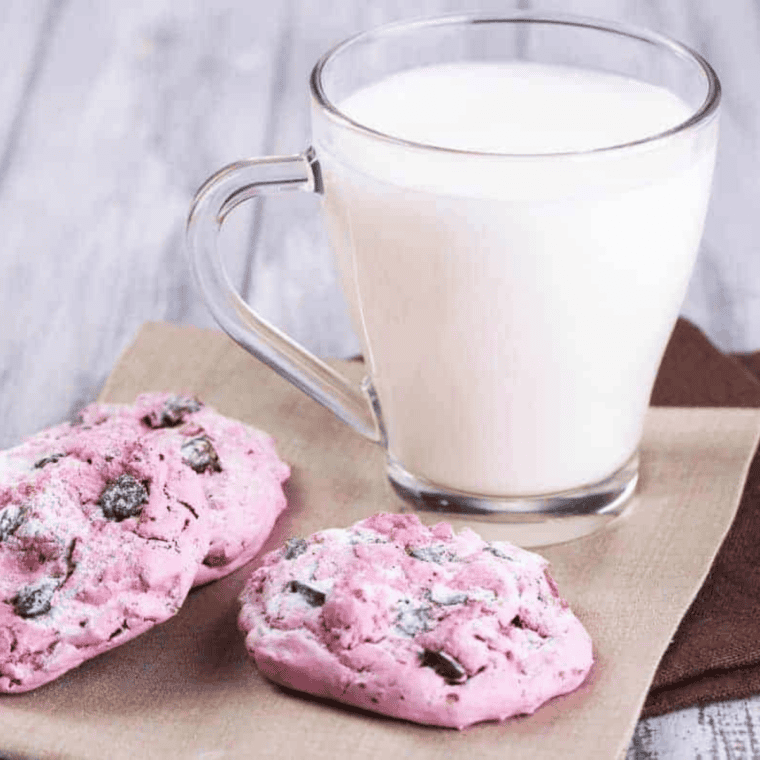 Scooping strawberry cake mix cookie dough into air fryer lined with parchment paper.