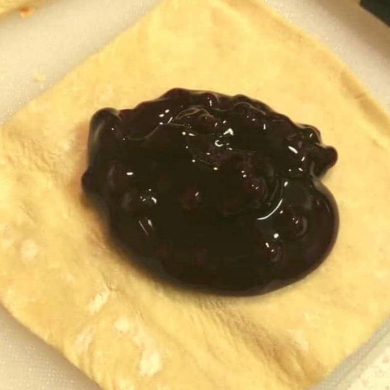 Thawed puff pastry sheets being cut into squares and rectangles on a floured surface.