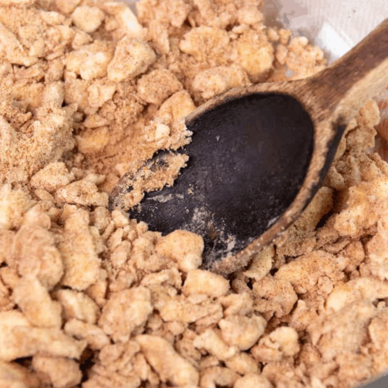 Mixing bowl with crumb topping ingredients for cinnamon crumb donuts, including brown sugar, cinnamon, salt, butter, and flour.