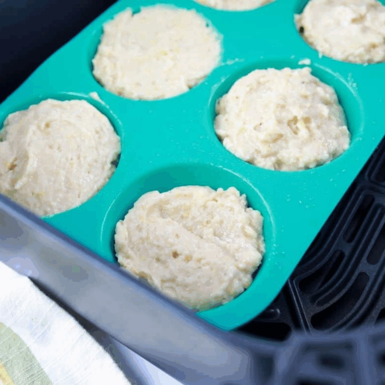 Pouring muffin batter into greased cups and placing in air fryer basket