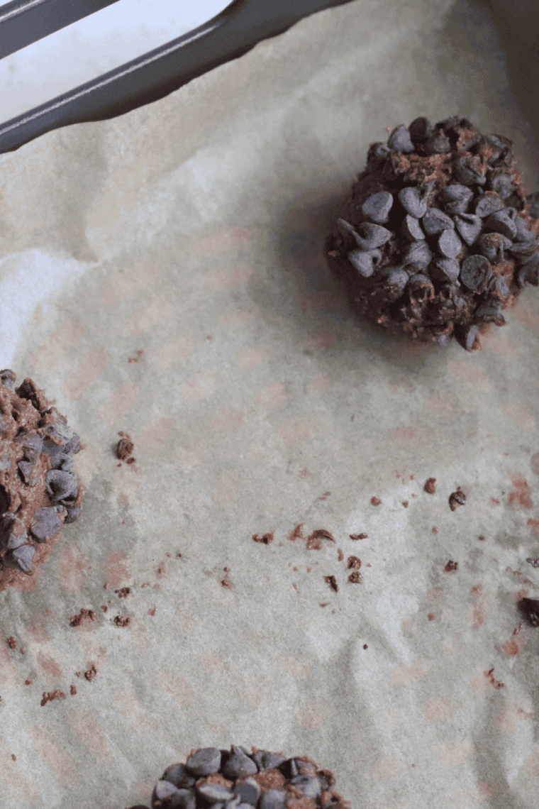 Flattened cookie dough balls arranged on a parchment-lined air fryer basket, ready to cook.