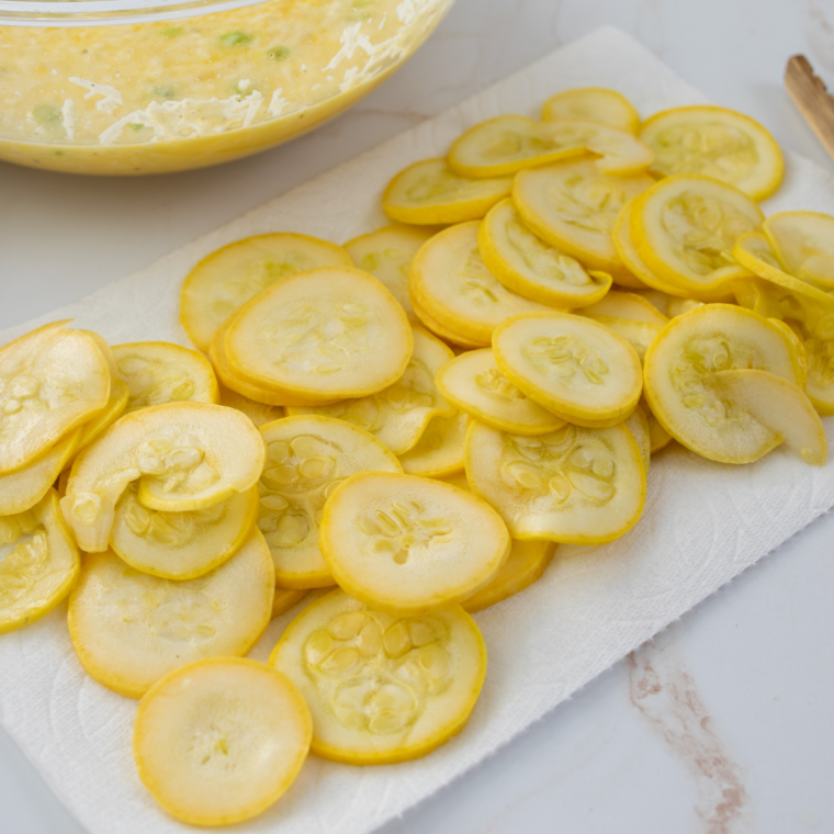 Yellow summer squash sliced into uniform half-inch rounds on a wooden cutting board
