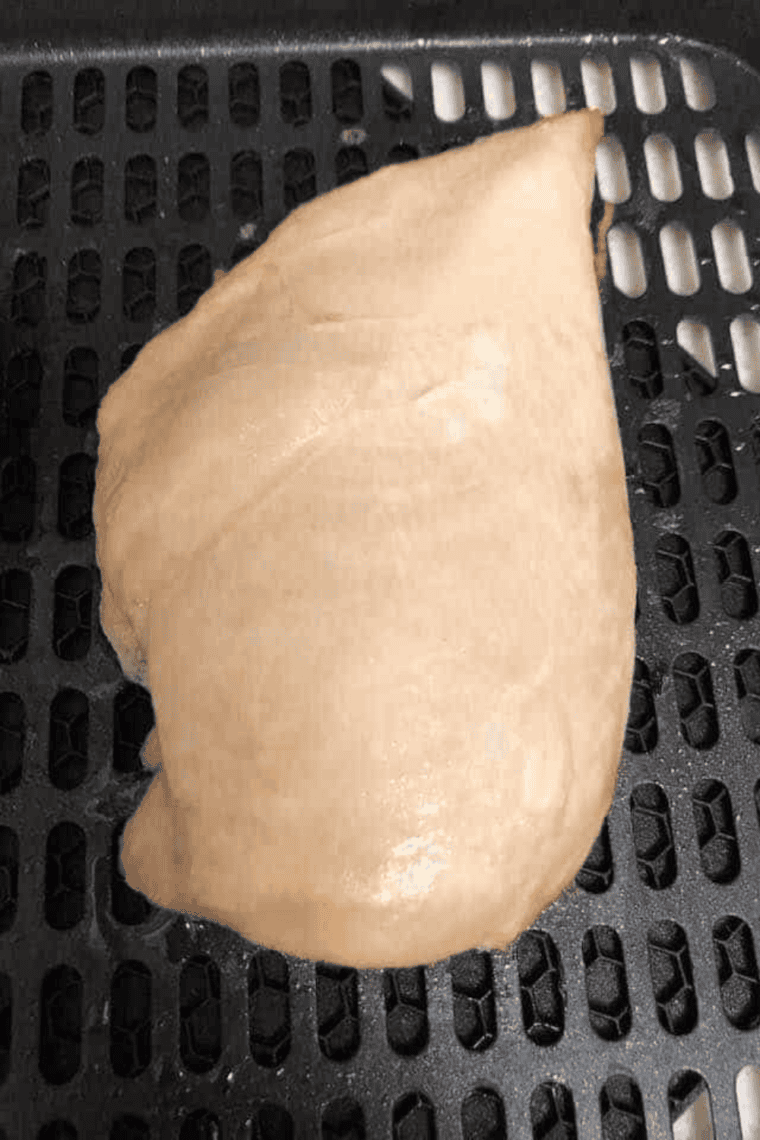 Seasoned boneless skinless chicken breasts in an air fryer basket ready to cook