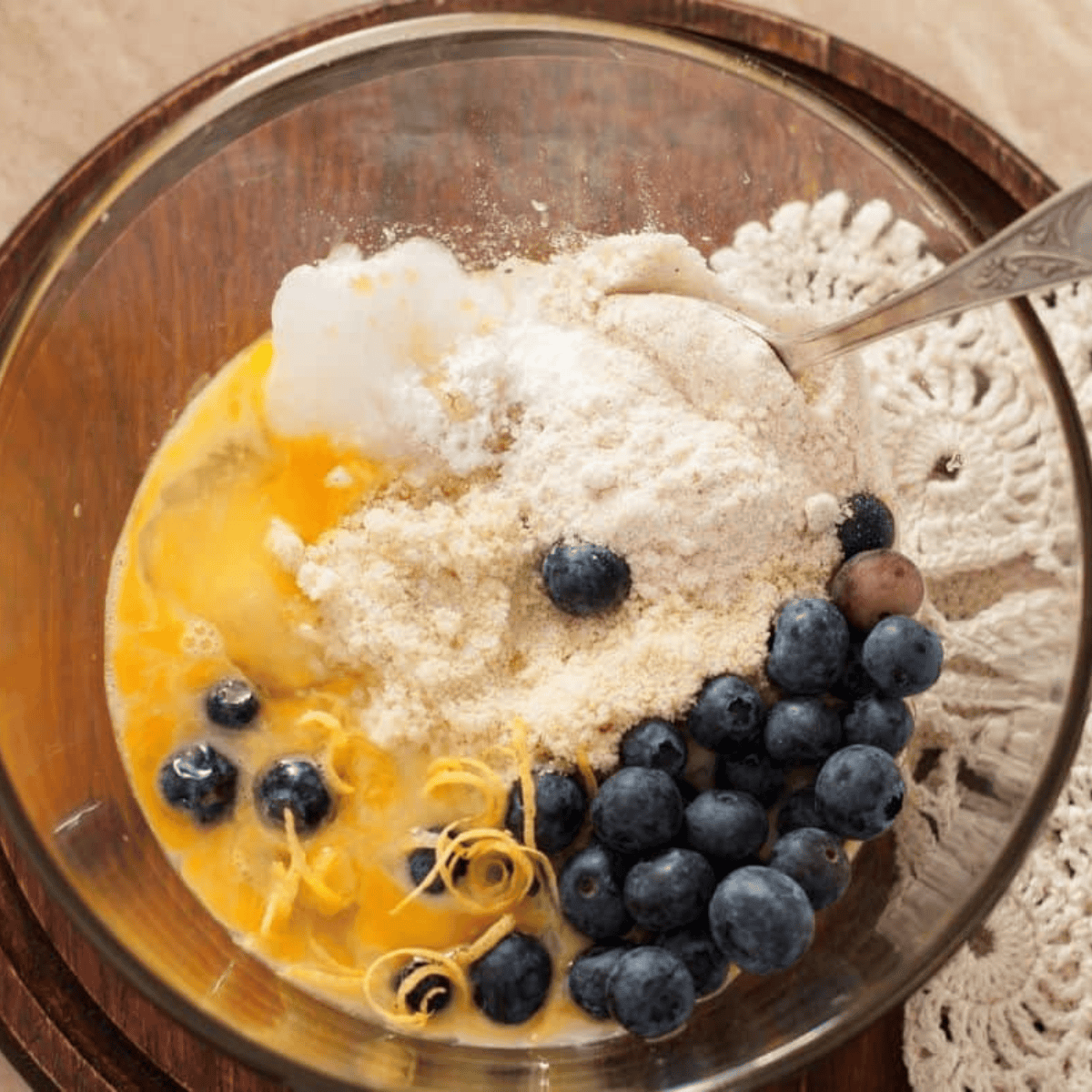 Mixing butter and sugar, adding eggs, milk, flour, baking powder, salt, lemon juice, then folding in fresh blueberries