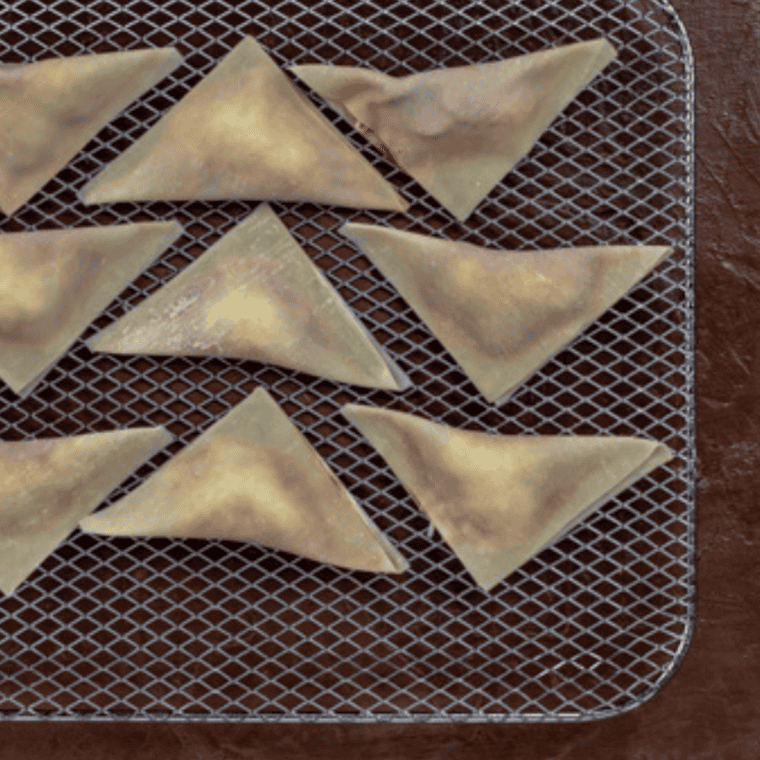 Apple pie wonton folded into a triangle with edges sealed by pressing with a fork on a wooden cutting board