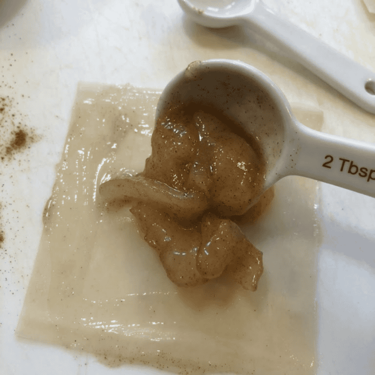 Square wonton wrapper laid flat on a wooden cutting board with a tablespoon of cinnamon apple filling spooned into the center