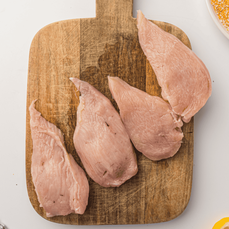 Boneless chicken breast being pounded thin with a meat mallet before breading for the air fryer
