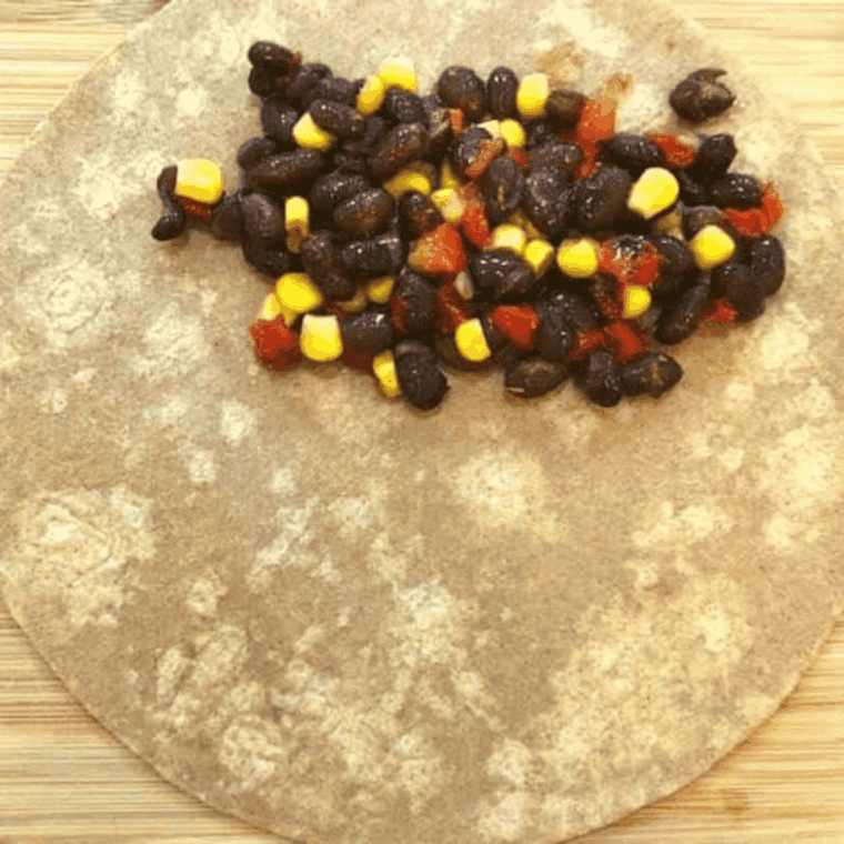 Spreading black bean and corn filling onto one side of a tortilla