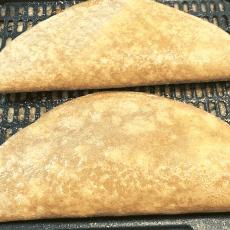 Folded quesadillas cooking in air fryer, sprayed with olive oil for crispy golden texture