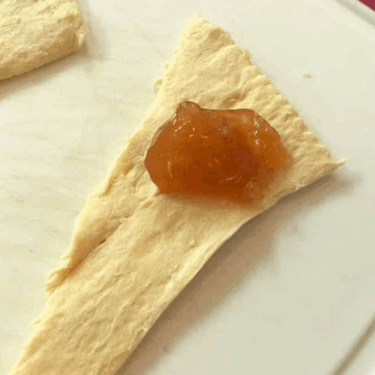 Crescent dough rolled around a spoonful of apple pie filling, ready to bake