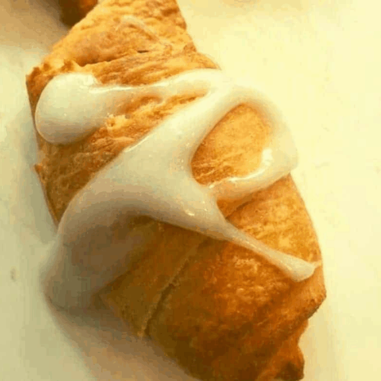 Small bowl of powdered sugar and milk glaze being drizzled over cooled apple crescent pastries.