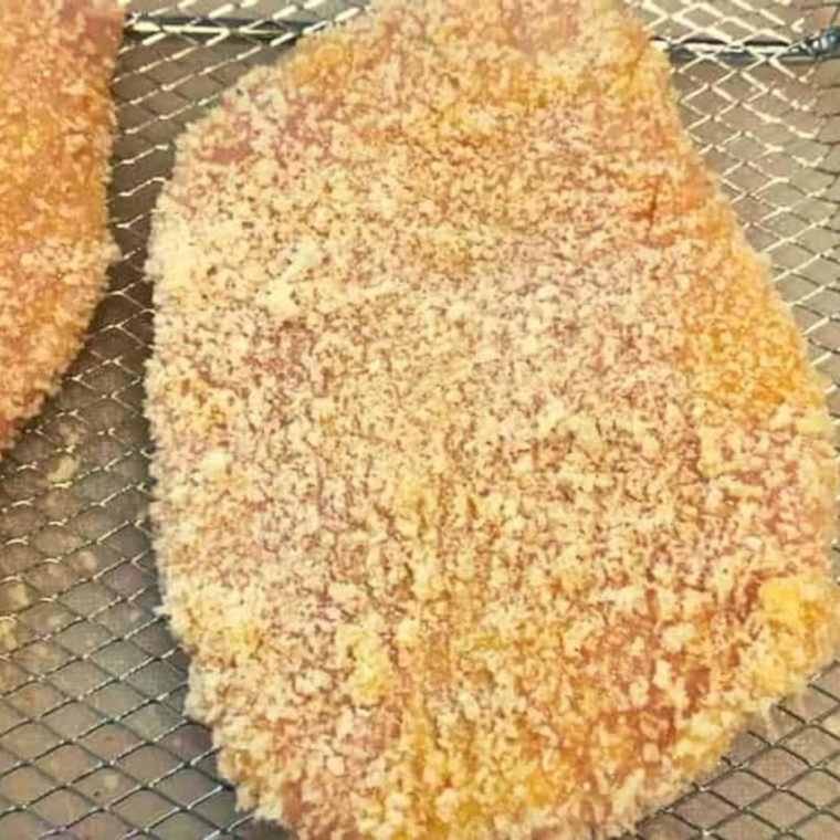 Hands pressing golden toasted panko and parmesan onto an egg-coated chicken cutlet
 