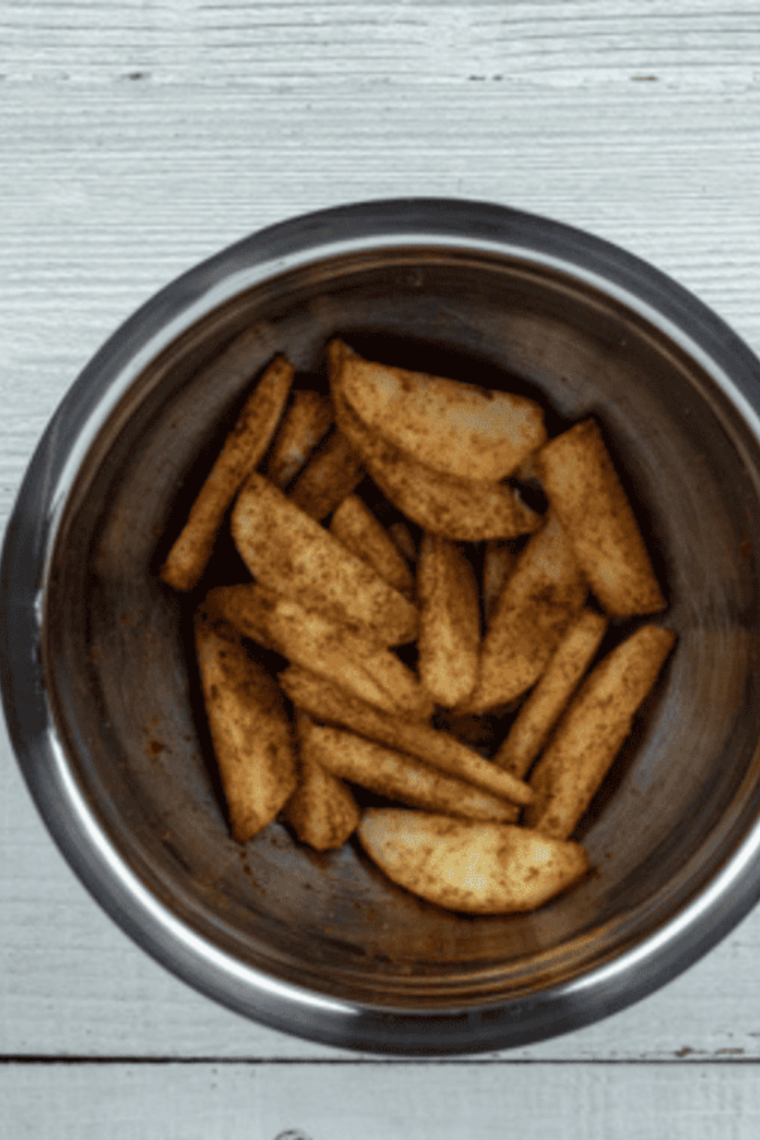 Thinly sliced peeled apples being tossed in cinnamon and sugar in a bowl until evenly coated for caramelized flavor.