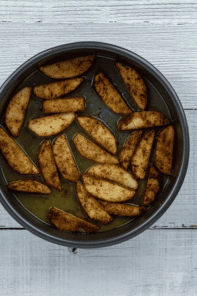 Butter melting and sizzling in air fryer safe pan then cinnamon sugar apples arranged in single layer over melted butter.