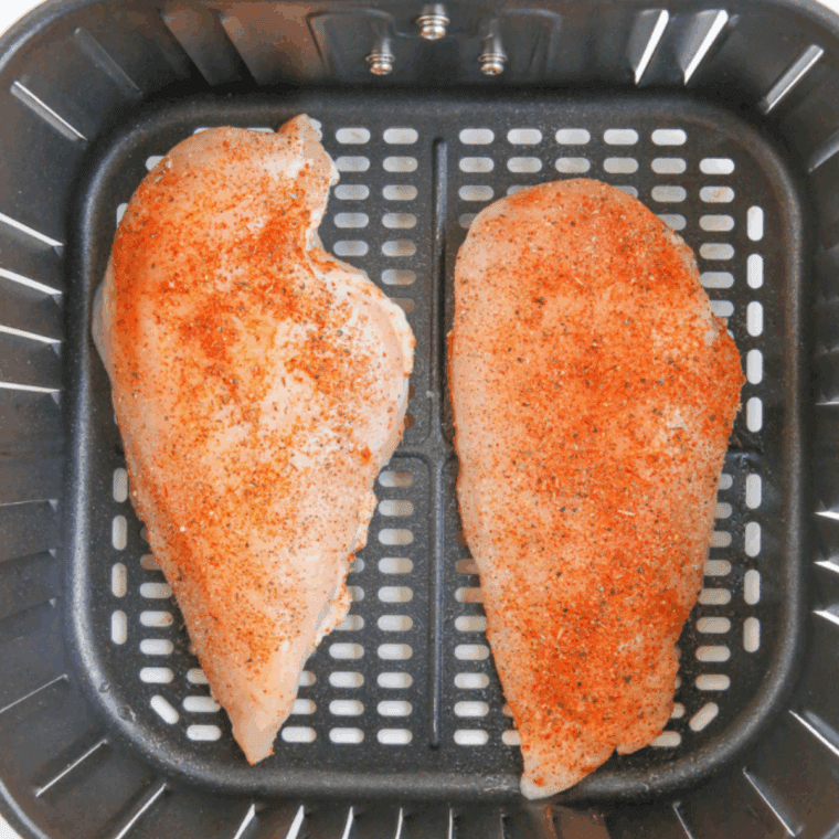 Chicken breasts placed in an air fryer basket, cooking at 380°F, flipped halfway for even golden-brown doneness.