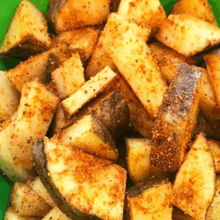 Potato slices in a large bowl, coated with olive oil, salt, pepper, and maple BBQ seasoning.