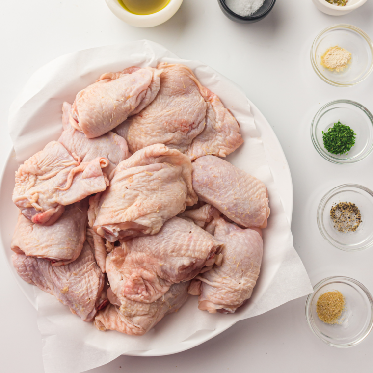 Ingredients for air fryer pesto chicken thighs including chicken thighs, basil pesto, olive oil, lemon, garlic powder, salt, and pepper