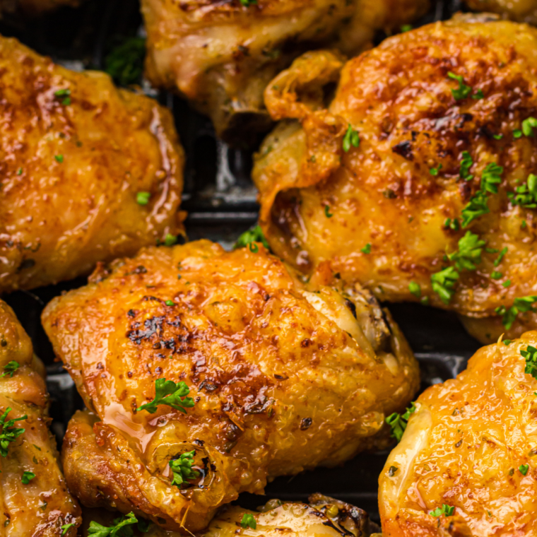 Air fryer pesto chicken thighs in a black air fryer basket, coated in green basil pesto with browned crisp edges
