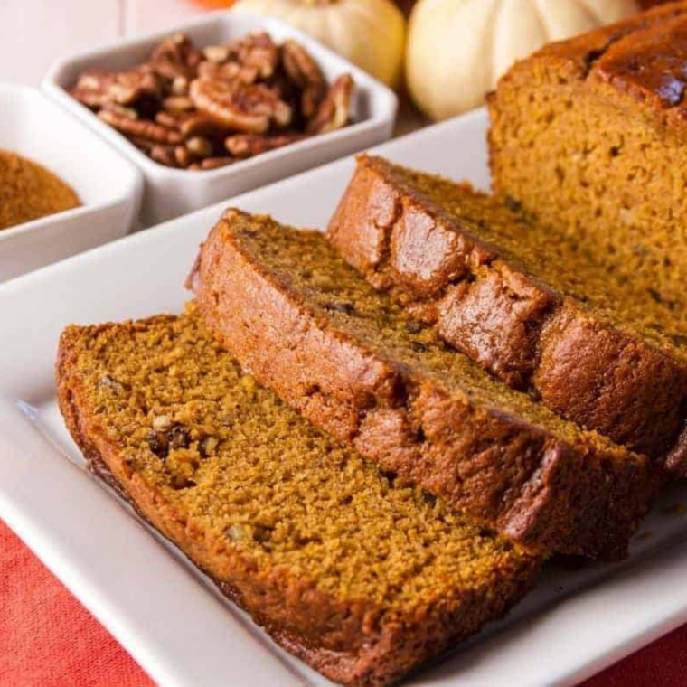 Four mini loaves of air fryer pumpkin nut bread topped with toasted pecans, cooling on a wire rack
