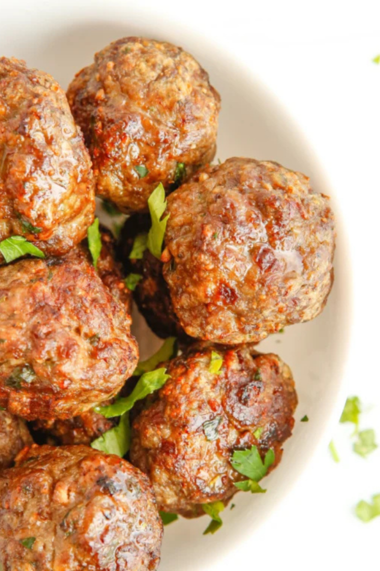 Glazed BBQ meatballs in an air fryer basket, shiny and caramelized with a sticky barbecue coating.