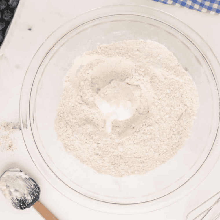 Mixing bowl with flour, baking powder, salt, sugar, and cinnamon being combined with shortening and buttermilk to form biscuit dough.