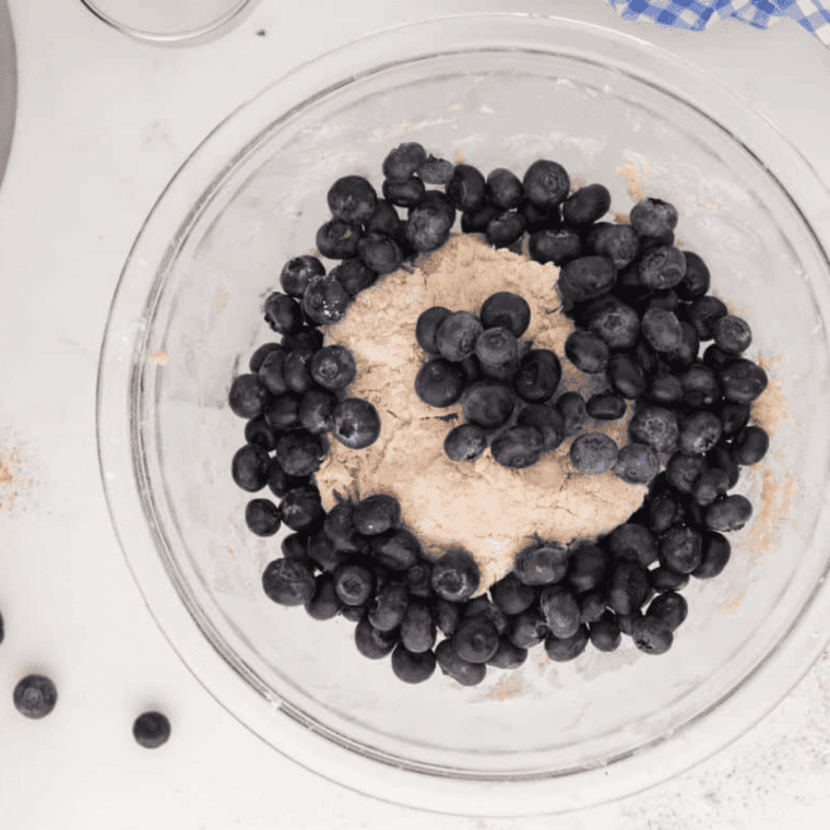 Folding fresh blueberries into biscuit dough by hand, then rolling out on floured surface with rolling pin.