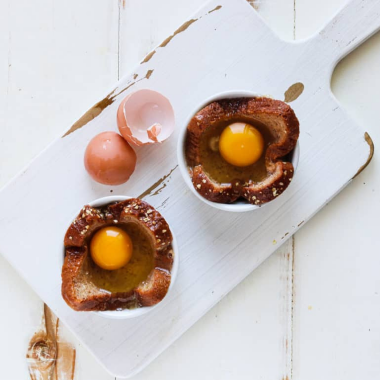 Egg cracked into bread center topped with shredded cheese in ramekin, ready for air fryer