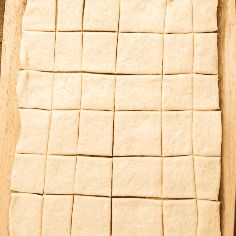 Cutting thawed puff pastry dough into 3x4 square or rectangular pieces using a pizza cutter on a flat surface.