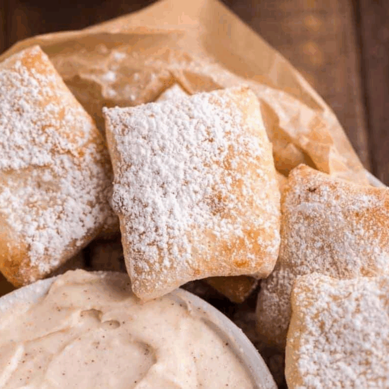 A serving plate piled high with golden, puffy Air Fryer Puff Pastry Beignets dusted heavily with white powdered sugar.