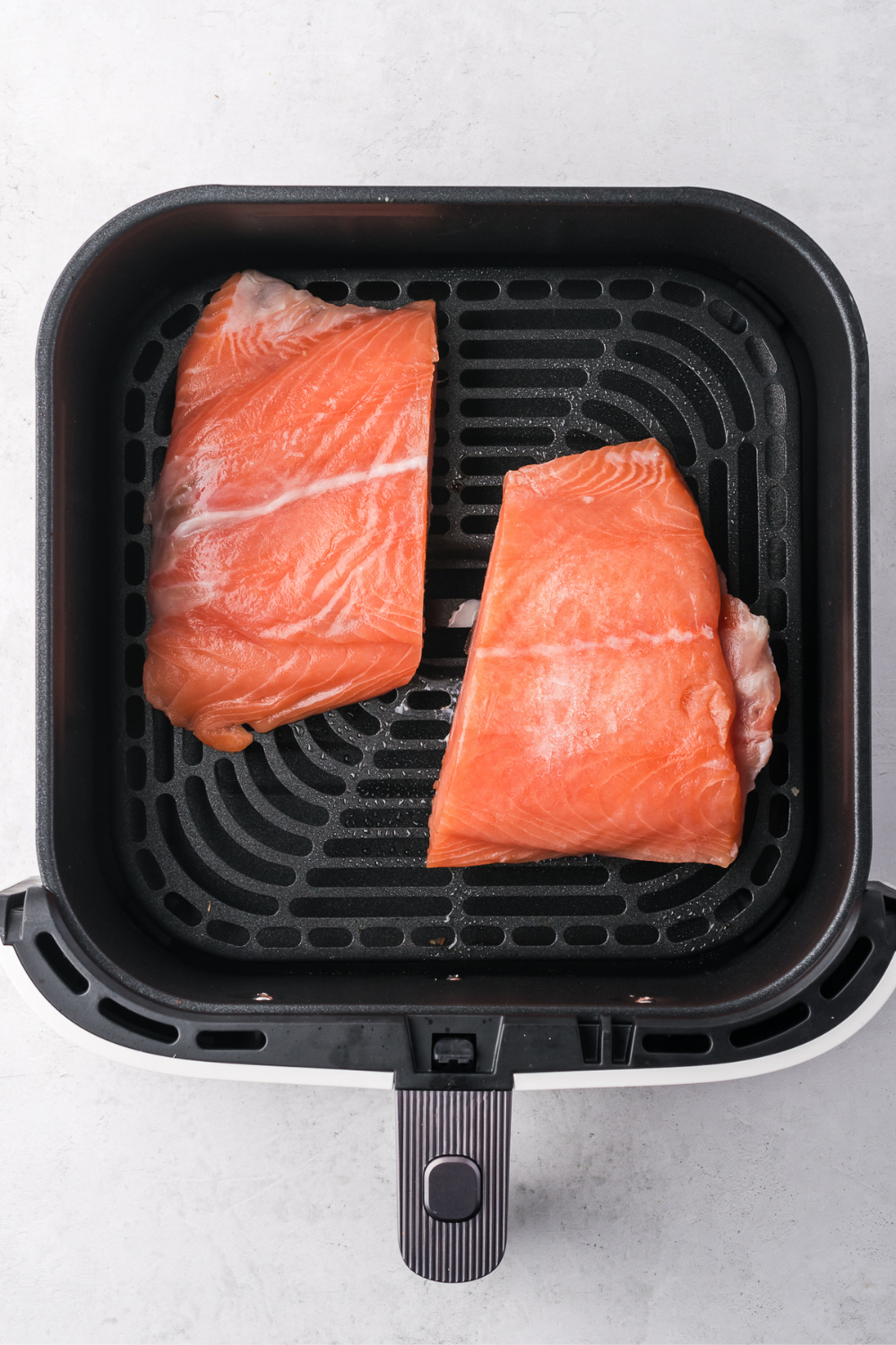 Patting frozen salmon dry to remove surface ice before air frying to prevent excess steam and ensure proper browning and texture